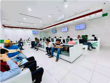 Busy Amer Center waiting area with customers and digital display screens in Dubai.